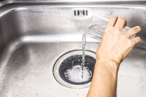 A person in Springfield, IL pouring an unknown liquid substance down their kitchen sink drain that is preventing water from draining correctly.