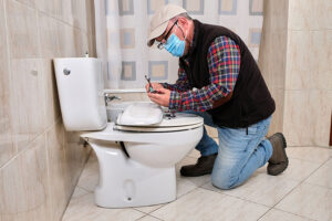 A professional plumber is determining the cause of a leaky toilet in this Springfield, IL residence.
